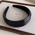 Vista macro de diadema gruesa de cuero negro con textura plisada en bandeja elegante - Negro