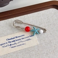 Detailopname van vintage schoenbedeltje met houten kralen en zeester op beige stof - Rode Kraal Blauwe Zeester Speld Stijl (27304-2)