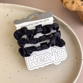 Detailed macro view of three black satin scrunchies neatly displayed on a card packaging - Set of 3 / Black (27346F)