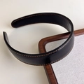 Close-up of black leather headband with contrast orange stitching on wooden tray - Black