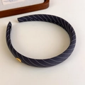 Detailaufnahme eines gestreiften Stoff-Haarreifens mit goldenem Hand-Made-Metallemblem - Grau