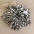 Detailansicht eines silbernen Metallic-Scrunchies mit Faltenstruktur auf Steinhintergrund - Silbergrau