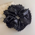 Detail eines großen schwarzen Scrunchies mit Metallic-Glanz und Rüschenrand-Textur - Hellschwarz
