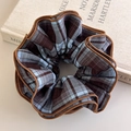 Close-up of a plaid hair scrunchie with four-layer overlock edges on a beige book - Brown Plaid (27407B)