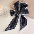 Detail of a paisley print silk scarf tied in a bow next to candles and vintage books - Black Paisley Border