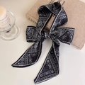 Detail shot of a black and white paisley silk scarf tied as a bow for handbag styling - Geometric Black Paisley