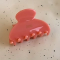 Detailed close-up of coral pink acetate hair claw clip with golden logo on beige surface - Korean Pink