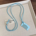 Detalle de cerca del colgante de peine azul claro y cuenta plateada en collar tejido - Estilo Cuadrado Azul