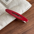 Detalle macro de una pinza para el pelo roja ovalada calada sobre una tela de lino - Estilo Rojo (27428A)