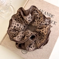 Dettaglio di un grande elastico per capelli in raso leopardato su un libro vintage - Leopardo Caffè Chiaro