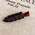 Detalle de pinza de pelo vintage ondulada en negro pulido y rojo oscuro sobre lino - Negro