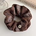 Dettaglio macro di un elastico per capelli paisley marrone con bottone su sfondo vintage - Caffè Scuro