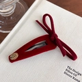 Detail of red velvet bow hair clip with gold Smile Happy charm on a woven background - Red