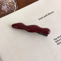 Dettaglio ravvicinato della molletta per capelli ondulata in pelle rossa su un libro - Fermaglio a Becco d'Anatra Ondulato Rosso (27459A)