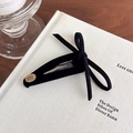 Close-up of black velvet bow hair clip with gold logo on a minimalist background - Black