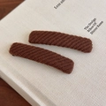 Close-up of two brown knitted rectangular hair clips on a white book with rich fabric texture - Brown
