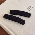 Pair of retro black knitted hair clips with woven texture on a white book cover - Black