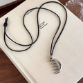 Primer plano de un collar con colgante de peine plateado sobre un libro con cordón negro fino - Peine Plateado con Cadena de Cordón Negro
