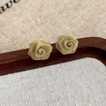 Detailaufnahme goldener Rosenohrringe aus Kupfergeflecht auf einem Holztablett - Gold