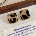 Gros plan de boucles d'oreilles léopard vintage avec monture dorée sur tissu - Carré Léopard Clair
