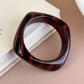 Macro shot of marble-textured reddish-brown acrylic square bangle leaning on a white book - Deep Red