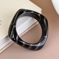 Dettaglio del bracciale quadrato in acrilico tartarugato su decorazione di libri minimalisti - Grigio Nero