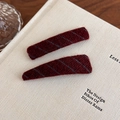 Detail view of burgundy wool hair clips with gray diagonal stitching on a book - Burgundy