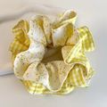 Détail d'un chouchou en tissu à carreaux et fleurs jaunes sur un plateau blanc - Style Patchwork Fleuri Vichy Jaune Blanc (26858B)