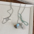 Détail du collier à billes argenté avec pompon bleu clair et pendentif en métal ajouré - Cacahuète Argentée