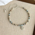 Close-up of blue beaded bracelet with silver shell pendant on beige linen display - Seashell Charm (27030A)