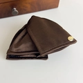 Detailed close-up of dark brown satin fabric texture with a round gold metal logo plate - Brown Coffee
