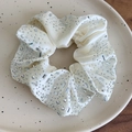 Makroansicht eines cremefarbenen Satin-Scrunchies mit glänzenden Strasssteinen - Cremeweißer Haargummi