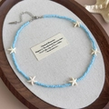 Dettaglio di collana di perle blu con ciondoli a stella marina su vassoio in legno - 27060 Collana Perline Stella Marina Blu