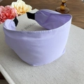 Vista detallada de una diadema ancha de tela lila con elástico negro sobre decorado - Violeta Claro