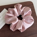 Detail of pink satin scrunchie with embossed rose pattern on brown wood surface - Pink