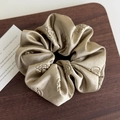 Detailed close-up of champagne gold satin scrunchie with rose jacquard on dark wood surface - Brown