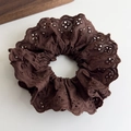 Close-up of a dark chocolate lace scrunchie with floral cutout detailing on white surface - Brown