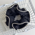 Detail of a black pleated hair scrunchie with cream borders inside a white wire basket - Black