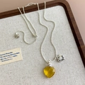 Détail du pendentif cœur ambré et de la chaîne à billes argentée sur plateau en bois - Coeur Jaune