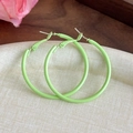 Close-up of bright lime green macaron-style hoop earrings on a textured beige background - Green