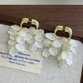 Detail von Muschelblüten-Ohrhängern mit Goldhaken auf rustikalem Vintage-Hintergrund - Cremeweiß und Gold