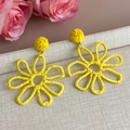 Gros plan de boucles d'oreilles fleurs en raphia jaune avec texture tressée artisanale - Style Jaune