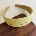 Detail eines gelben Polka-Dot-Haarreifens mit Schleifenstickerei auf edlem Holzdisplay - Gelb
