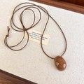 Dettaglio di collana vintage con ciondolo in pietra marrone su vassoio di lino - Caffè