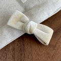 Close-up of cream velvet bow hair clip detail on rustic canvas and wooden surface - Beige