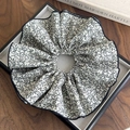 Dettaglio di un elastico per capelli scrunchie floreale con foglie nere e bordi rifiniti - Base Bianca Con Fiori Neri
