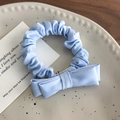 Dettaglio dell'elastico per capelli in raso azzurro con fiocco su un piatto di ceramica bianco - Blu