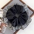 Gros plan d'un chouchou à rayures avec froufrous sur un support gris au style minimaliste - Noir