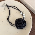 Nahaufnahme des schwarzen Satinrosen-Chokers mit weißen Perlen auf einem Dekoteller - Schwarz