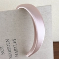 Detail eines rosa Satin-Haarreifs mit schimmerndem Perlmutt-Finish auf einem Buch - Rosa